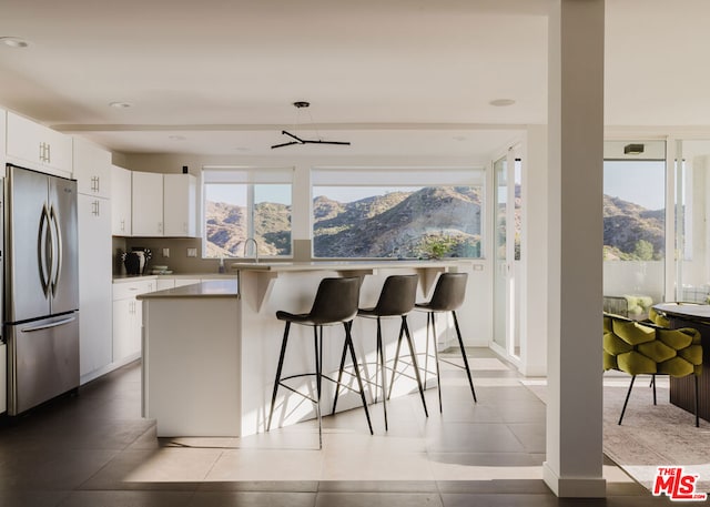 kitchen featuring white cabinetry, stainless steel fridge, a kitchen bar, a center island, and a mountain view