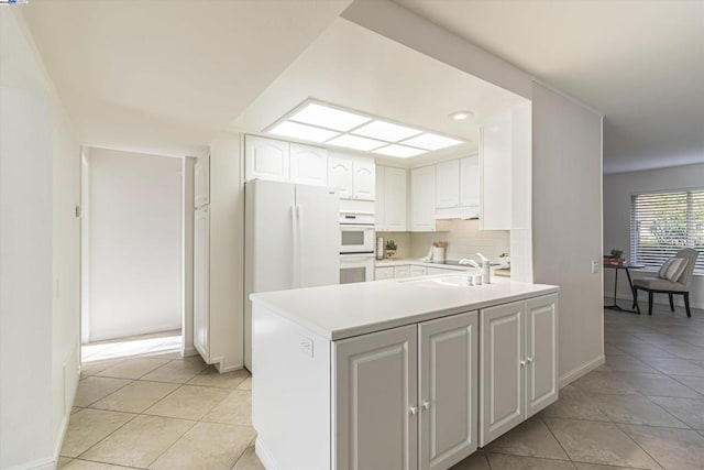 kitchen with tasteful backsplash, white cabinetry, sink, light tile patterned floors, and white appliances