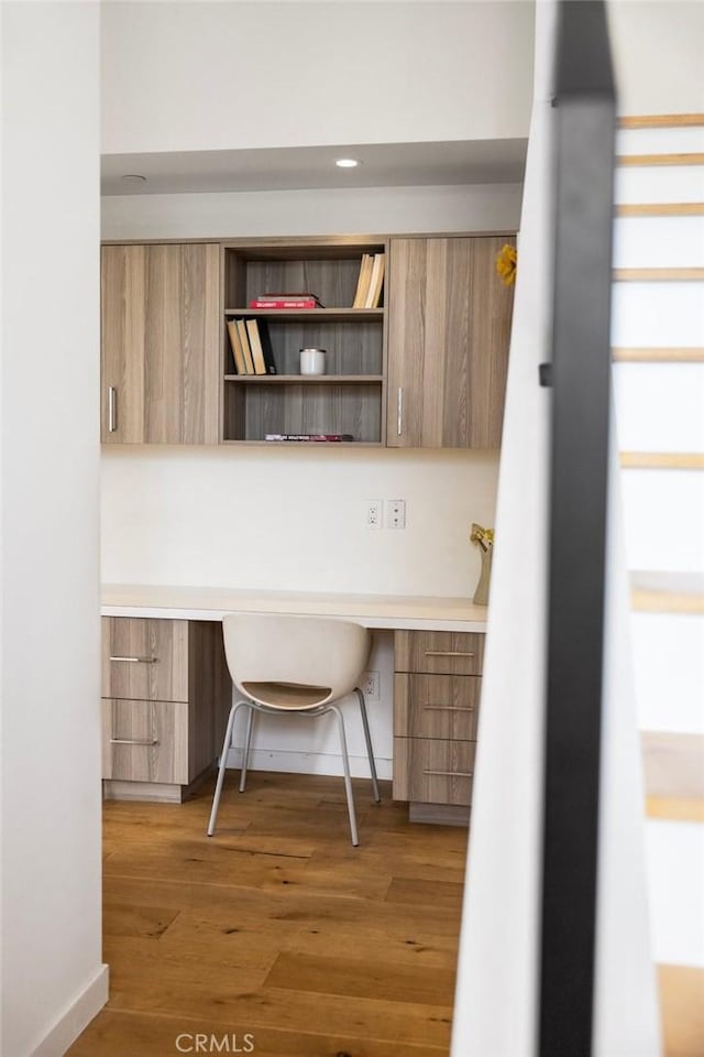 unfurnished office featuring hardwood / wood-style flooring and built in desk