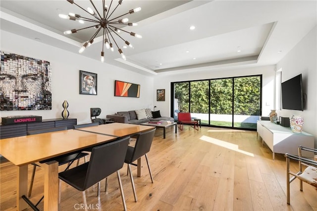 dining area featuring an inviting chandelier, light hardwood / wood-style floors, and a raised ceiling