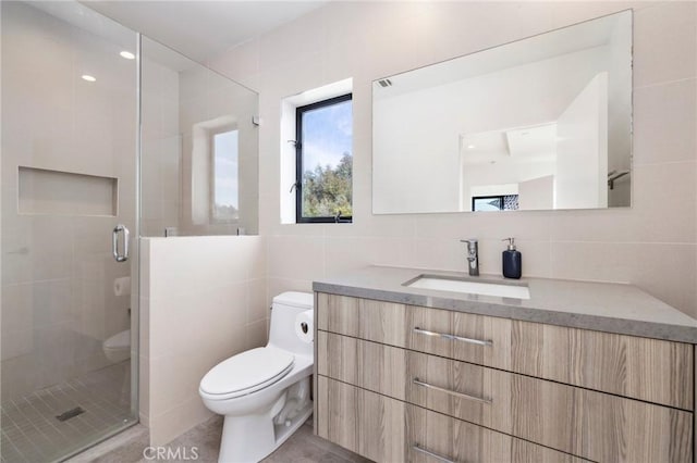 bathroom with tile walls, vanity, a shower with door, and toilet