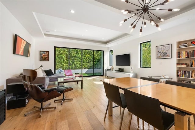 dining room featuring a raised ceiling, a chandelier, and light hardwood / wood-style floors