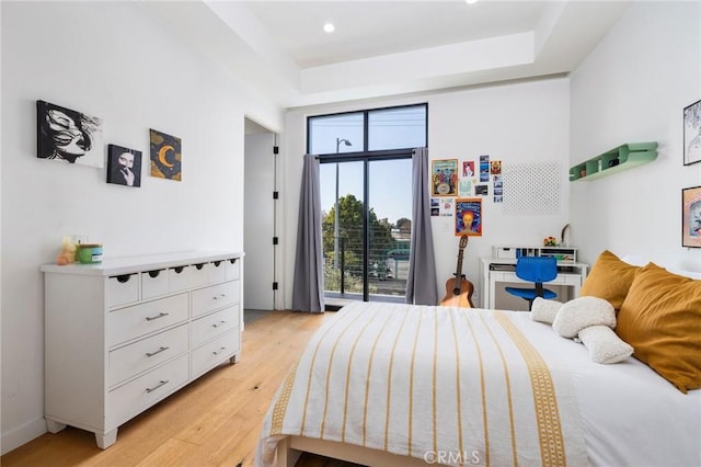 bedroom with access to exterior, light hardwood / wood-style floors, and a raised ceiling