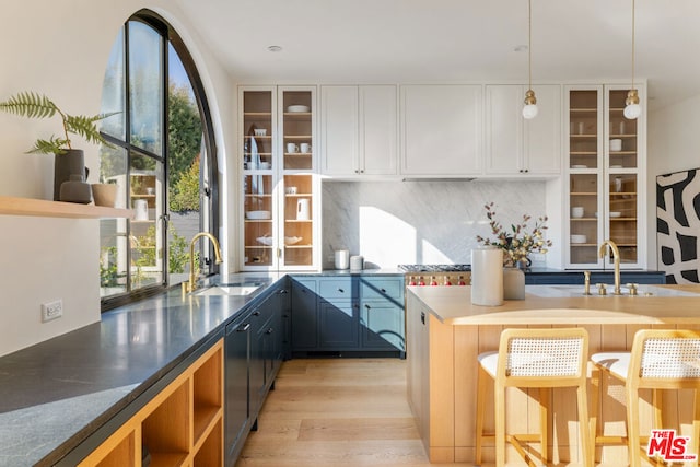 kitchen with decorative light fixtures, sink, a breakfast bar area, white cabinets, and light wood-type flooring