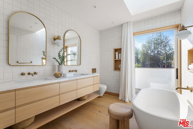 bathroom featuring wood-type flooring, toilet, tile walls, and a tub to relax in