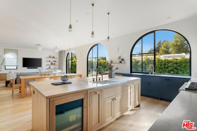 kitchen with sink, light hardwood / wood-style floors, a kitchen island with sink, and hanging light fixtures