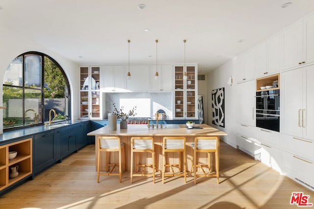 kitchen with decorative light fixtures, a center island with sink, blue cabinetry, and a kitchen bar