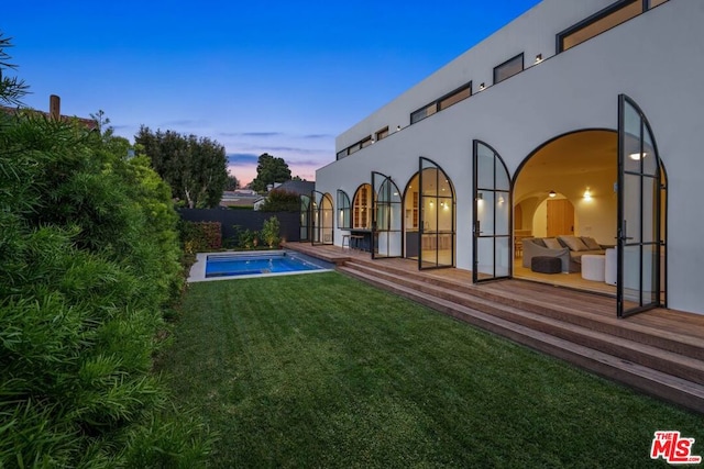 back house at dusk featuring a lawn and a patio