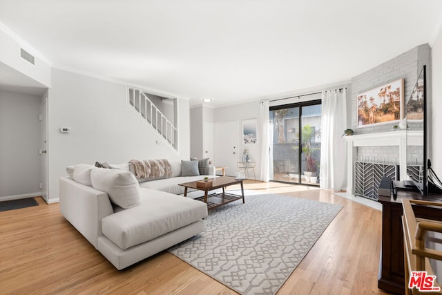 living room featuring a brick fireplace, light hardwood / wood-style flooring, and ornamental molding