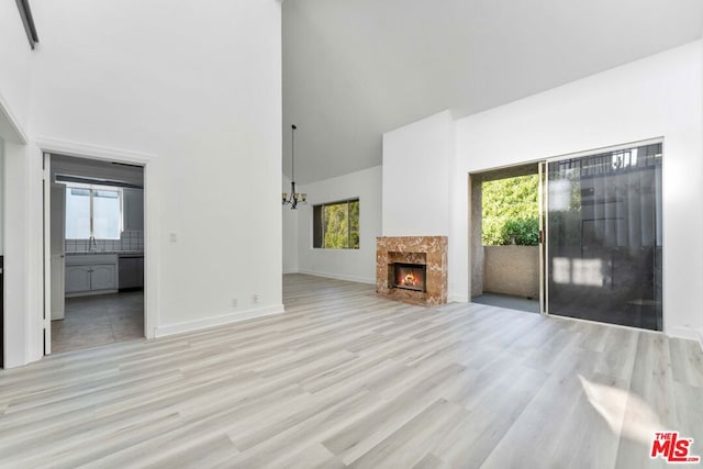 unfurnished living room featuring a towering ceiling, a healthy amount of sunlight, a high end fireplace, and light hardwood / wood-style flooring