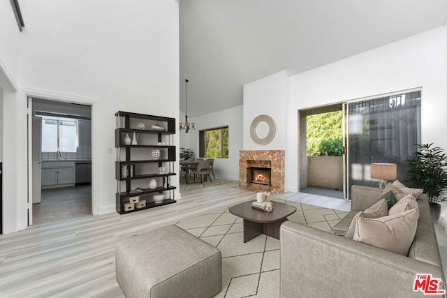 living room featuring a notable chandelier, a fireplace, light hardwood / wood-style floors, and a high ceiling