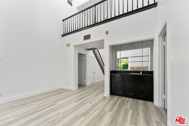 unfurnished living room with a towering ceiling, sink, and light wood-type flooring