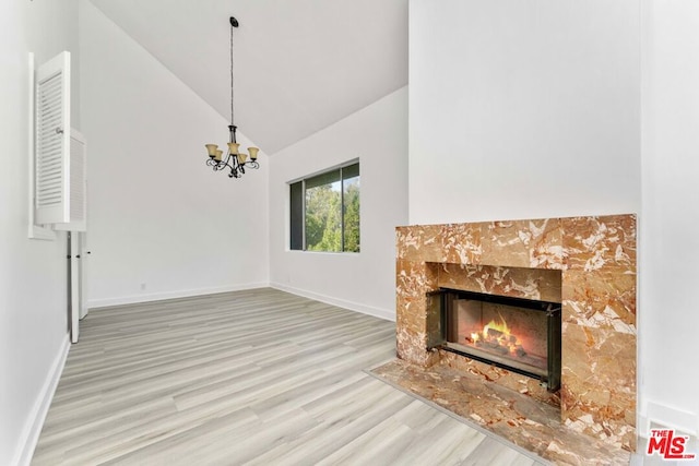 unfurnished living room featuring high vaulted ceiling, a fireplace, a chandelier, and light hardwood / wood-style floors