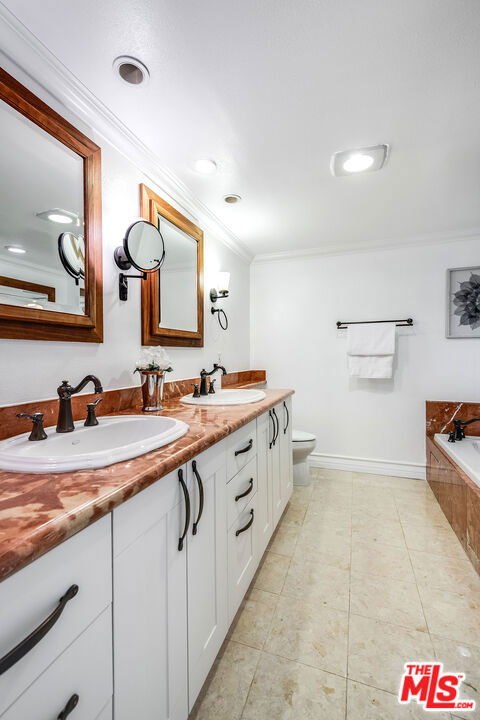 bathroom with tiled tub, vanity, ornamental molding, tile patterned floors, and toilet