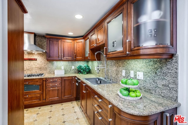 kitchen with tasteful backsplash, wall chimney range hood, light stone countertops, and sink