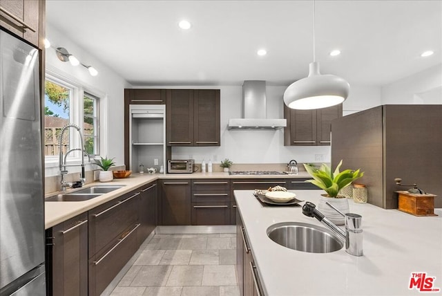 kitchen with pendant lighting, sink, wall chimney exhaust hood, and appliances with stainless steel finishes