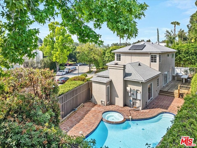 rear view of property with a swimming pool with hot tub and solar panels