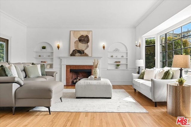 living room with built in shelves, a fireplace, crown molding, and hardwood / wood-style floors