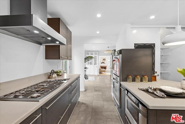 kitchen featuring decorative light fixtures, stainless steel gas cooktop, dark brown cabinets, and wall chimney range hood