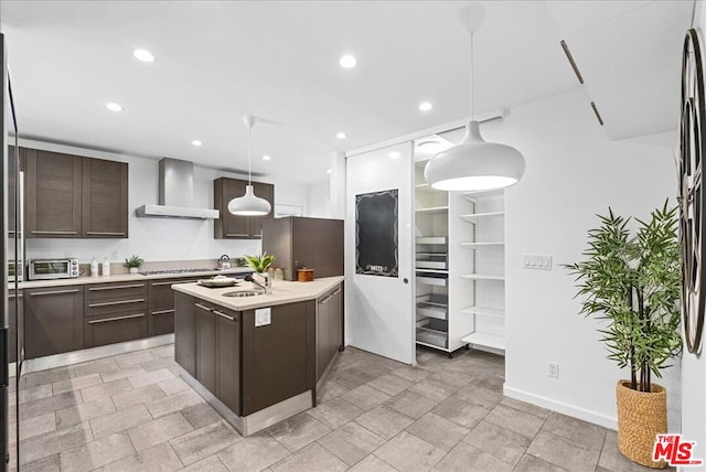 kitchen featuring dark brown cabinetry, hanging light fixtures, wall chimney exhaust hood, and appliances with stainless steel finishes