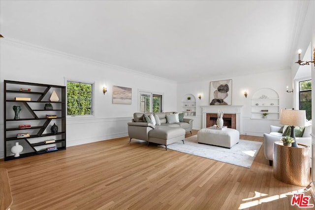 living room with built in shelves, an inviting chandelier, crown molding, light hardwood / wood-style flooring, and a fireplace