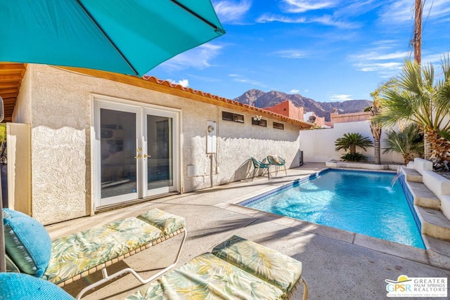 view of pool featuring pool water feature, a mountain view, a patio area, and french doors