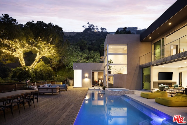 pool at dusk featuring an in ground hot tub, an outdoor hangout area, and a wooden deck