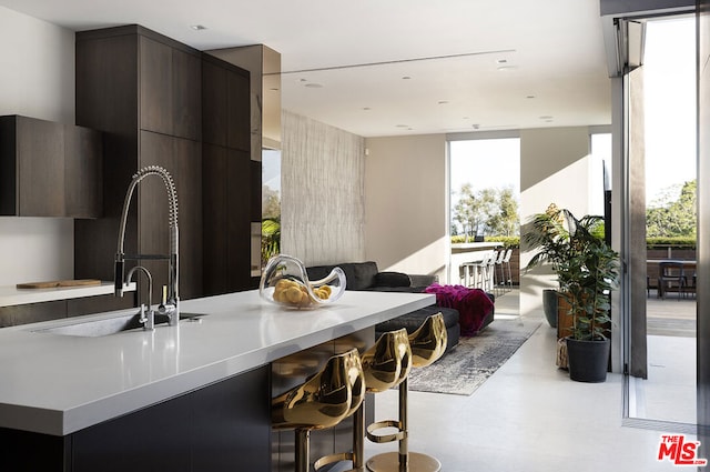 kitchen with dark brown cabinetry, sink, a kitchen bar, and a wall of windows