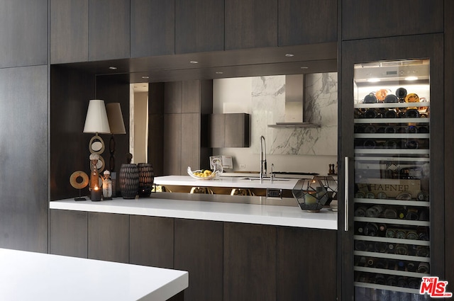 kitchen featuring wine cooler, wall chimney range hood, and dark brown cabinets