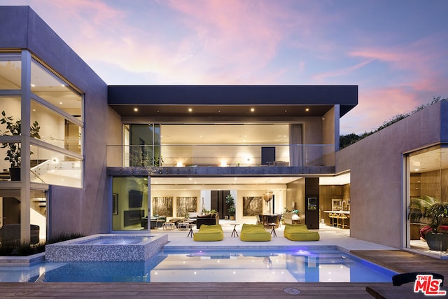 back house at dusk featuring a balcony, an outdoor hangout area, and a pool with hot tub