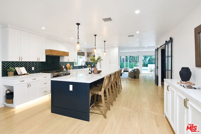 kitchen with custom exhaust hood, white cabinetry, decorative light fixtures, a kitchen island, and a barn door