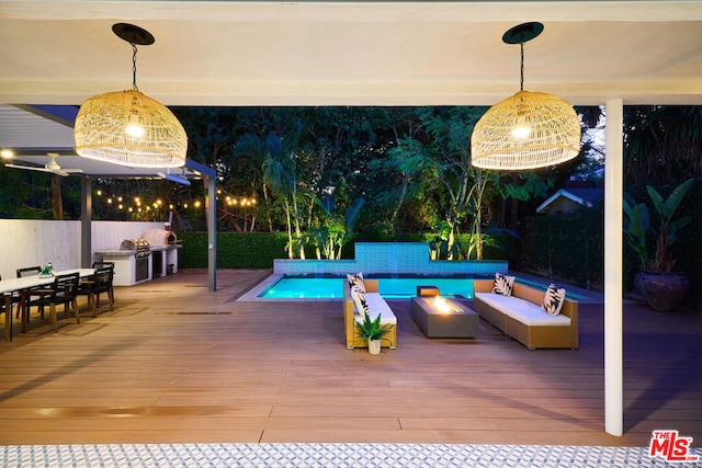 view of pool featuring a wooden deck, an outdoor hangout area, and exterior kitchen