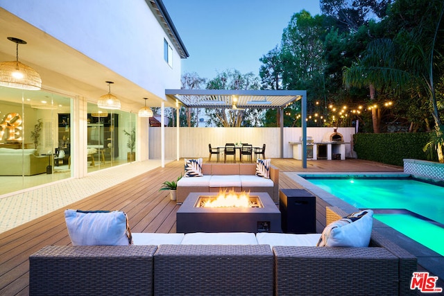 pool at dusk featuring area for grilling, an outdoor living space with a fire pit, a deck, and a pergola