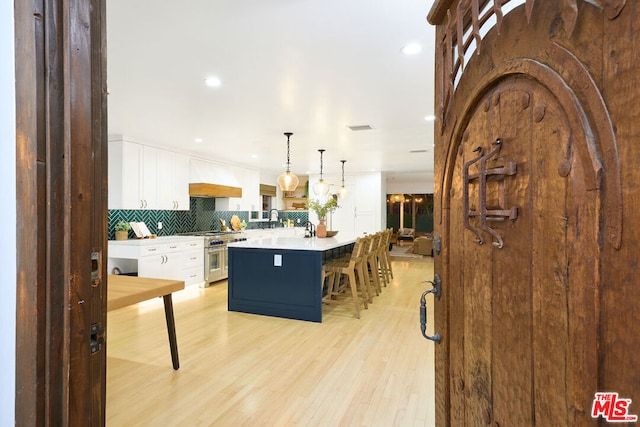 kitchen with high end stainless steel range, a center island, white cabinets, and decorative light fixtures