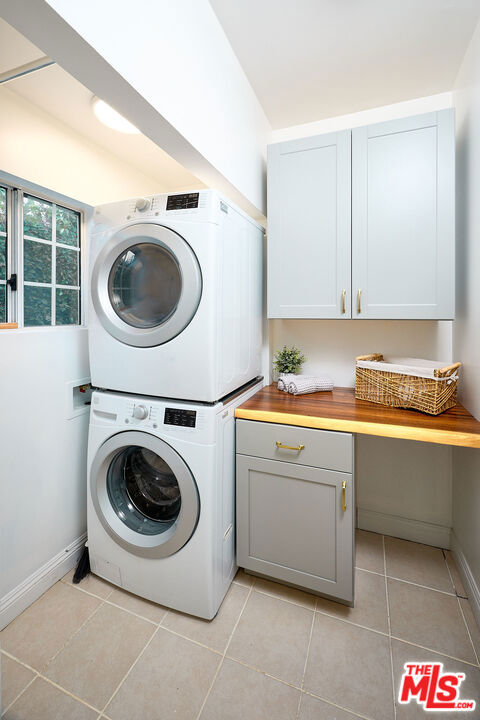 washroom featuring cabinets, stacked washer and clothes dryer, and light tile patterned floors