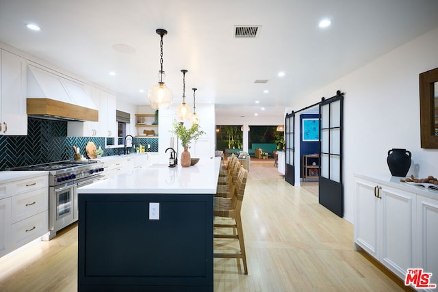 kitchen featuring pendant lighting, white cabinetry, custom range hood, a barn door, and range with two ovens