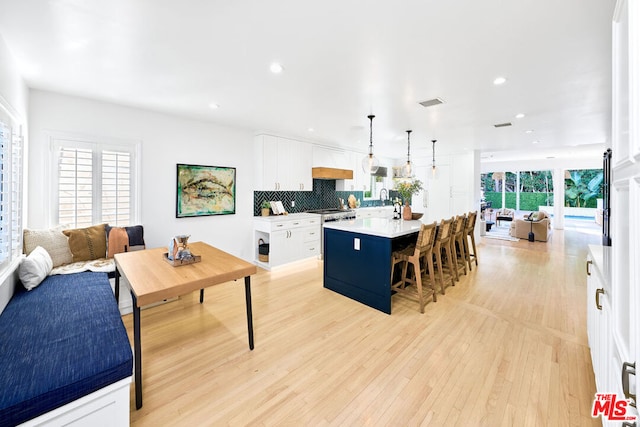 kitchen with white cabinetry, a kitchen breakfast bar, high end range, hanging light fixtures, and a kitchen island with sink