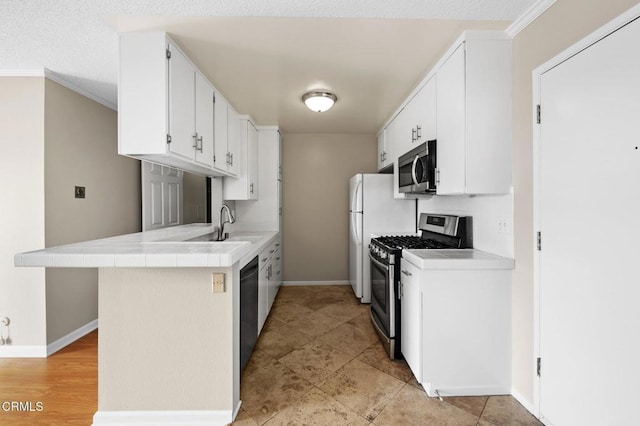 kitchen with appliances with stainless steel finishes, white cabinetry, sink, tile counters, and kitchen peninsula