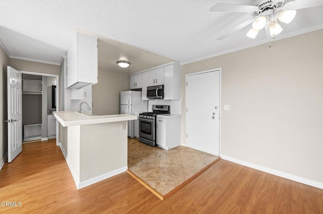 kitchen with appliances with stainless steel finishes, white cabinets, ornamental molding, light hardwood / wood-style floors, and kitchen peninsula