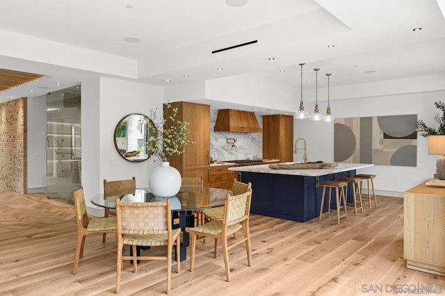 dining room with sink, a tray ceiling, and light hardwood / wood-style floors