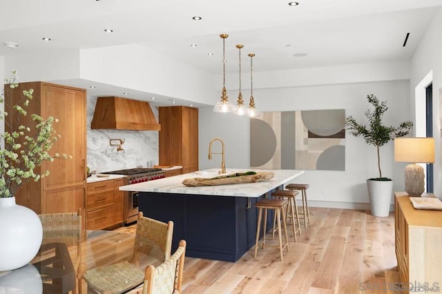 kitchen featuring high end stainless steel range oven, premium range hood, hanging light fixtures, tasteful backsplash, and a center island with sink