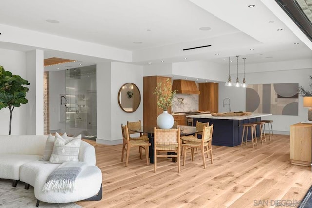 dining space with sink, light wood-type flooring, and a tray ceiling