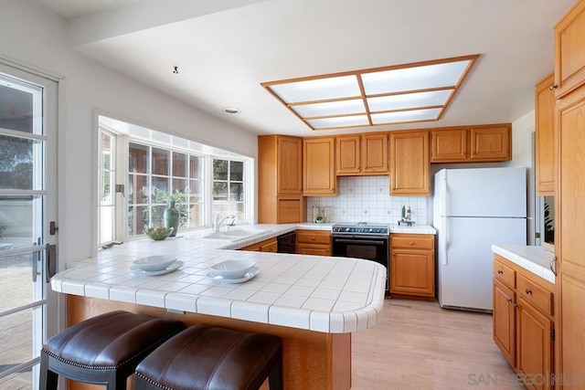 kitchen with a breakfast bar, sink, white fridge, range, and tile counters