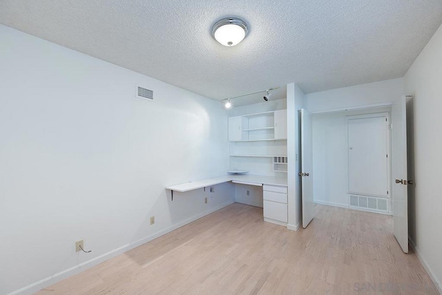 unfurnished office with track lighting, built in desk, light hardwood / wood-style flooring, and a textured ceiling