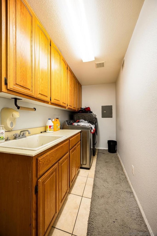 laundry room with sink, cabinets, washing machine and clothes dryer, a textured ceiling, and light tile patterned flooring