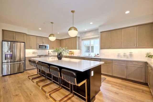 kitchen featuring light hardwood / wood-style flooring, appliances with stainless steel finishes, a kitchen breakfast bar, a kitchen island, and decorative light fixtures