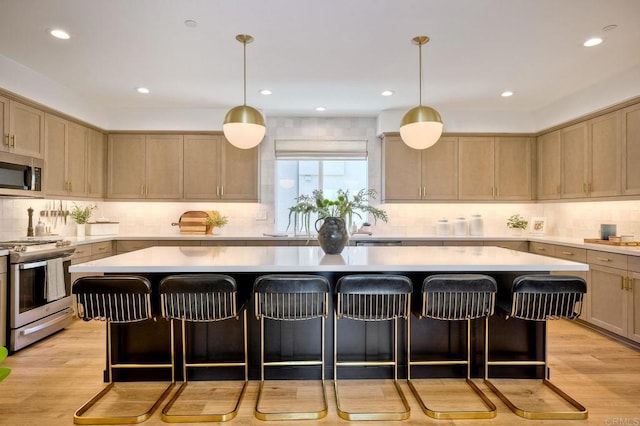 kitchen with appliances with stainless steel finishes, a center island, hanging light fixtures, and light hardwood / wood-style flooring