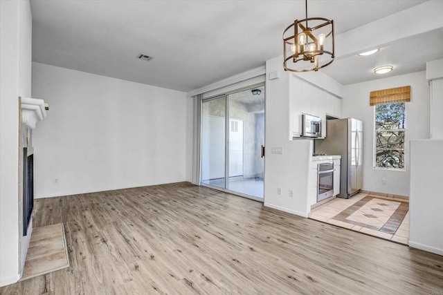 unfurnished living room featuring a notable chandelier and light hardwood / wood-style flooring