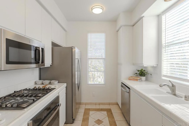 kitchen featuring tile countertops, white cabinetry, sink, light tile patterned floors, and stainless steel appliances