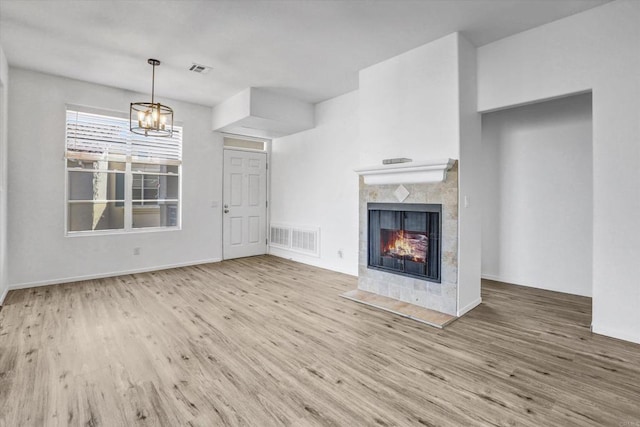 unfurnished living room featuring a fireplace, a chandelier, and light hardwood / wood-style flooring